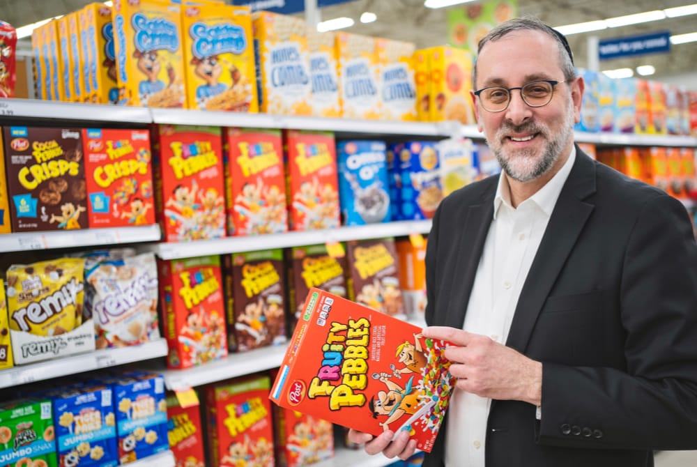 Yosi Heber standing in cereal aisle in grocery store holding box of Fruity Pebbles