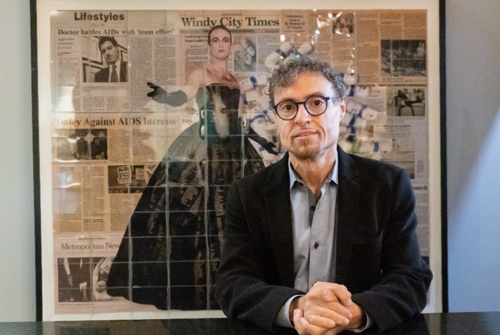 Daniel Berger posing in front of newspaper articles about his work on the AIDS epidemic